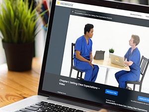 Person watching a Medbridge microlearning course on a laptop, featuring two clinicians in conversation during a training video.