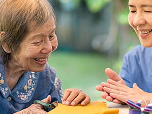 Occupational therapist supporting an older adult in a craft activity, demonstrating motor learning strategies after stroke.