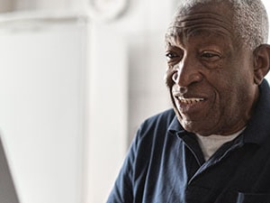 Older adult patient smiling while using a laptop for virtual care, representing digital tools that support patient engagement.
