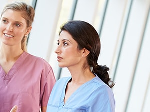 Three medbridge professionals in scrubs chat in a hallway with large windows.
