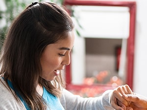 A young woman assists an older woman with a bracelet indoors, smiling near a mirror and plant.