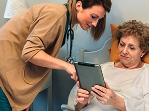 A healthcare professional presents information on a tablet to an elderly patient in bed, exemplifying medbridge's digital care.