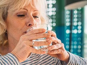 Elderly woman in a striped shirt drinks water with a person comforting her with a hand on her shoulder in a medbridge setting.