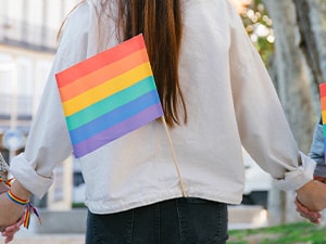 People in a park holding hands with rainbow flags on their backs.