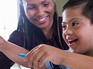 A woman and a child with Down syndrome smiling while crafting at a table.