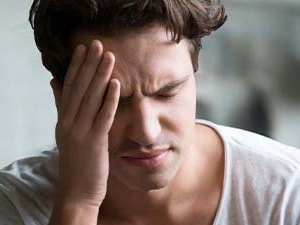 A person in a white shirt appears distressed with their hand on their forehead, background blurred.