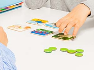 Two individuals organize picture cards and tokens on a table near a Medbridge book.