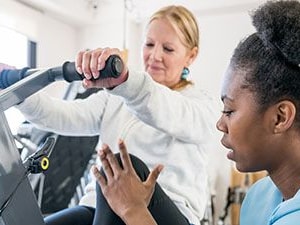 Physical therapist guiding a patient on an exercise bike during treatment for hypermobility spectrum disorder (HSD) or EDS.