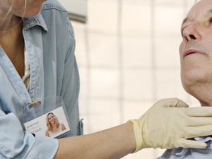 A healthcare professional in gloves examines an older man's neck in a clinic.