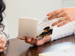 A person in a white sweater and another in scrubs discuss a medbridge pamphlet at a table with a folder.