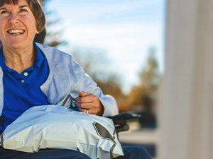 A Medbridge user in a wheelchair outdoors, smiling with a bag on their lap amidst sunny trees.