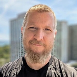 A man with a short beard and mustache in a black shirt stands outside by tall buildings, symbolizing the future of medbridge education.