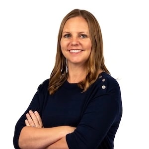 Woman with long brown hair in a navy top stands smiling with arms crossed, symbolizing medbridge healthcare education excellence.