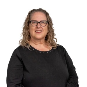 A smiling woman with curly hair and glasses stands against a white background, representing digital healthcare at medbridge.