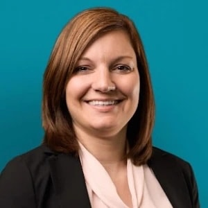 Smiling woman in black blazer stands before teal background, representing medbridge and digital healthcare.