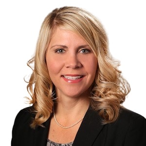A smiling individual with blonde hair and a black blazer represents Medbridge's digital healthcare passion.