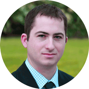 A man in a suit and tie outside with a green blurred background.
