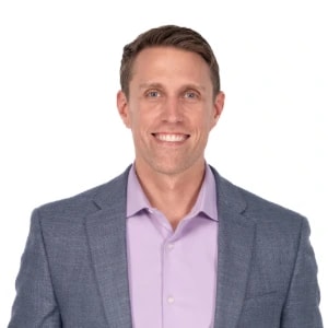 Man with short brown hair in a light purple shirt and gray blazer, smiling at the camera, representing medbridge.
