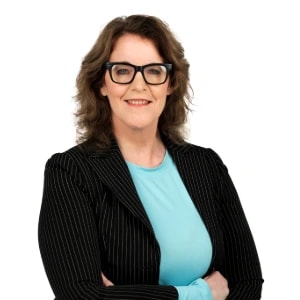 Woman with wavy brown hair, glasses, and pinstripe blazer smiles confidently, representing medbridge's role in digital healthcare.