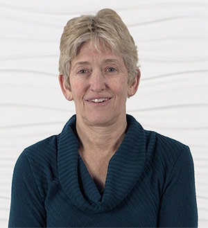 A person with short blonde hair in a teal sweater stands before a white textured background, symbolizing the future of digital healthcare by medbridge.
