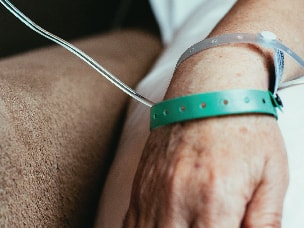 An arm with an IV line and medbridge wristbands on a bed.