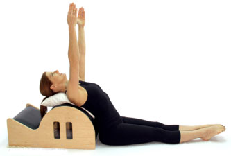 A woman in black workout attire lies on a yoga back bender, stretching her arms upward, representing hybrid care balancing body and mind.