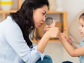 A woman and young girl sign to each other indoors.