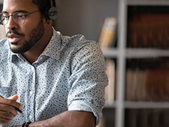 A man with headphones at a desk uses a laptop, representing Medbridge.