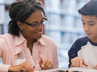 In a library, a woman and young boy read a book together.