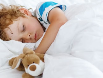 Child asleep in bed with a stuffed animal under a white duvet.