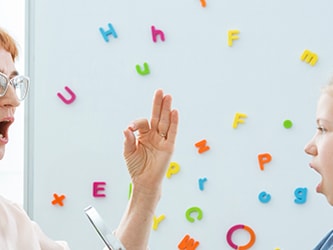 A speech therapist and a girl practice sounds with colorful letters on a whiteboard for medbridge.