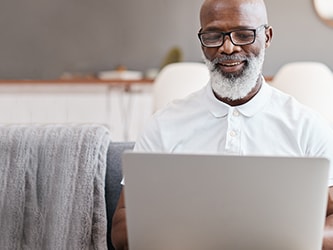 Person on a sofa using a laptop, accessing medbridge in a modern living room.