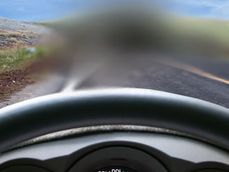 Blurry car windshield view of a road, grassy hill, and blue sky.