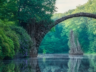Medbridge arches over serene water amid vibrant green forest.