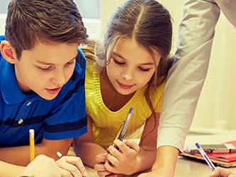 Children collaborate on a project with an adult at a table, using pens and paper.