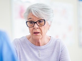An elderly woman with glasses talking to a medbridge healthcare worker.