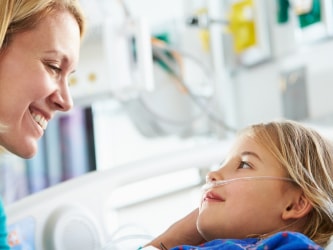 A woman smiles at a child in a hospital bed with a nasal cannula.