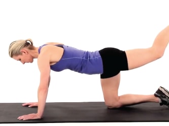 A person in workout clothes on a black mat does a donkey kick exercise for medbridge.