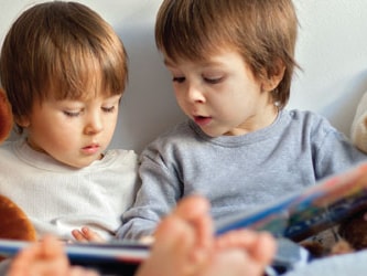 Two kids with stuffed bears read a book together.