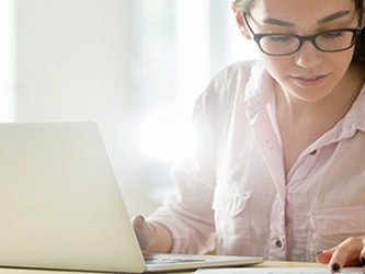A person using a laptop at a desk with medbridge materials and a small plant.