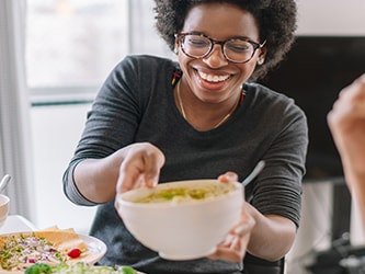 Two people enjoying a meal with fruits and salads in a bright room, one holding a bowl.