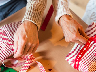 Two people in sweaters wrap gifts with red and white striped paper at a table.
