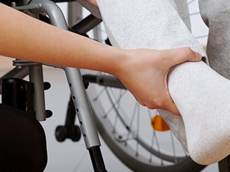 A Medbridge caregiver helps a wheelchair user by holding their leg in light gray sweatpants.