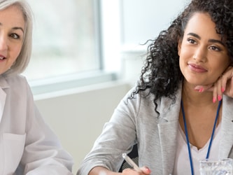 Two women, one older and one younger with curly hair, sit at a table actively engaged in conversation.