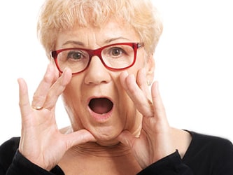 Surprised older woman with red glasses and short blonde hair against a white background.