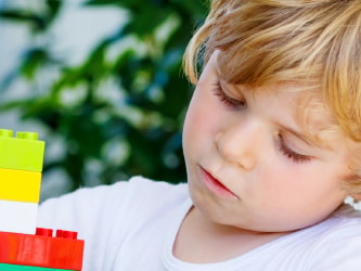 Child focused on assembling colorful blocks indoors.