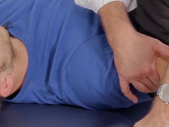 A person in a blue shirt receives shoulder therapy on a table.