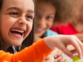 Children laughing together around a meal with water and carrots on the table.