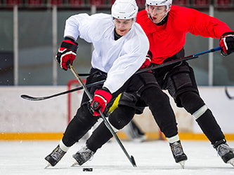 Two ice hockey players, one in white and one in red, compete for the puck as two others are visible in the background on an ice rink.
