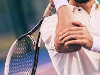Medbridge athlete in a white polo swings his racket on the tennis court.
